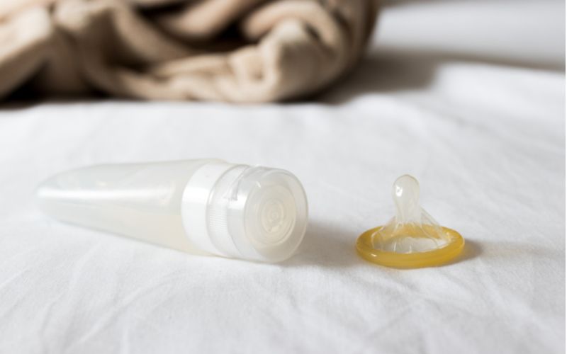 Lubrikační gely a sex, lubrikační láhev a kondom na posteli